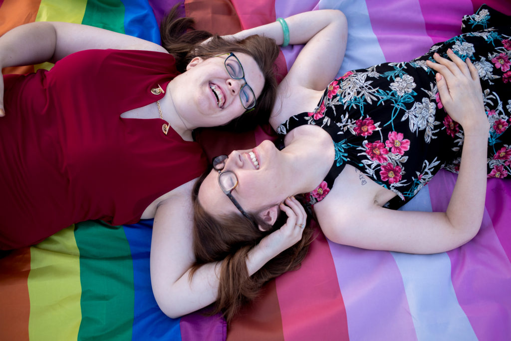 two women lay together laughing on the gay and lesbian flags